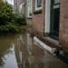 Nederlandse woning na hevige regenbui met water op straat als voorbeeld van klimaatschade en woonverzekering.